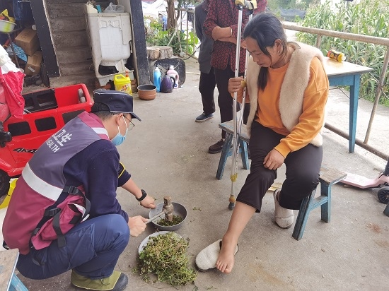 成中医救援队员将草药捣碎后外敷在村民脚踝处。成中医供图